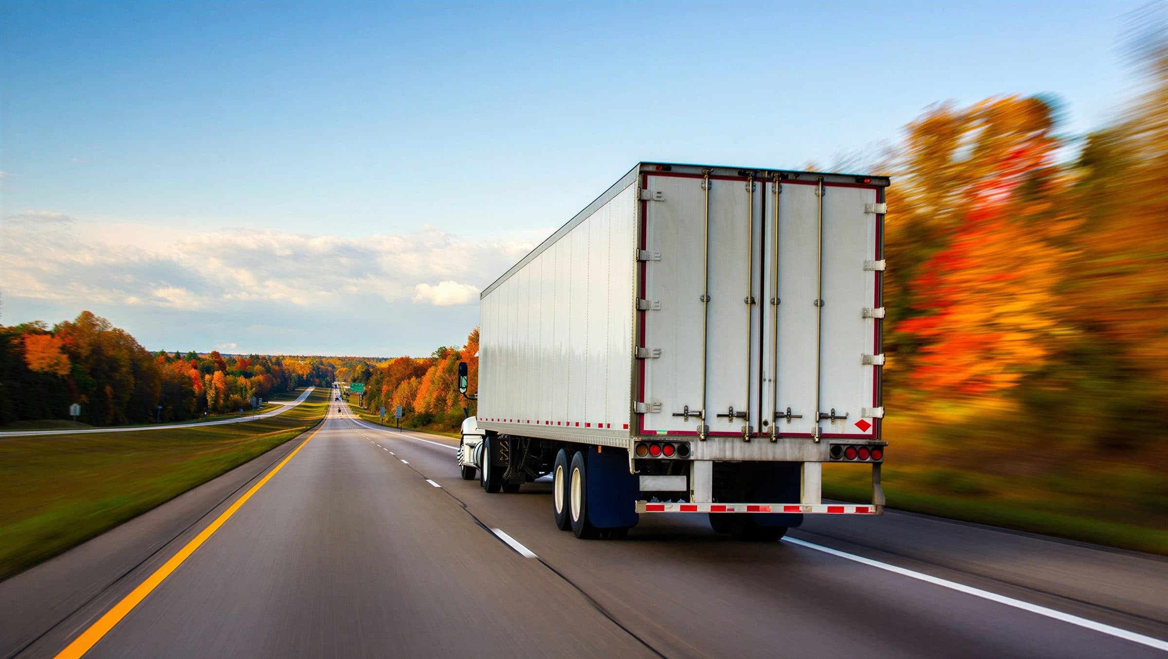 Tractor-trailer speeding down a highway lined with autumn trees